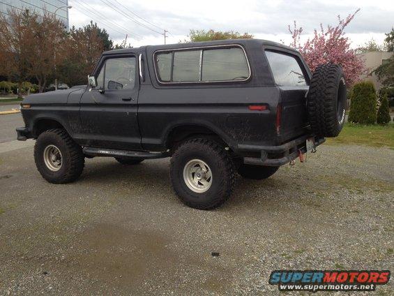 Black Ford Bronco with a spare tire mounted on the rear, parked on a gravel lot