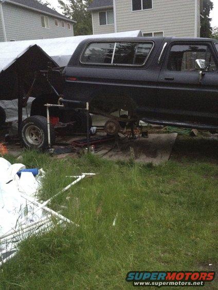 Black Ford Bronco with rear axle removed, parked under a tarp