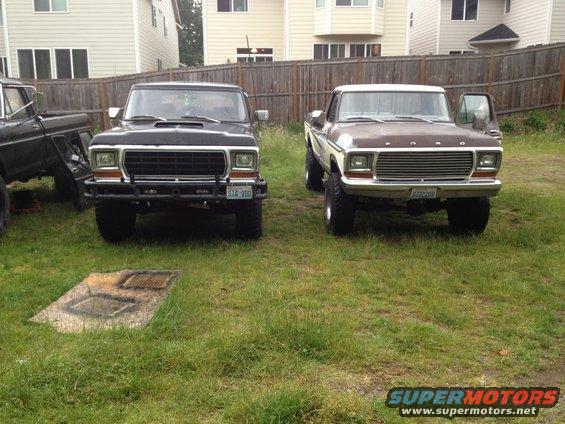 Two Ford trucks parked in a grassy yard. The one on the right is a 1979 Ford Bronco