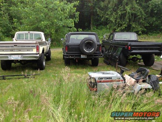 Rear view of a 1979 Ford Bronco, a 1970s Ford pickup, and another black Ford pickup. A Craftsman mower is in the foreground