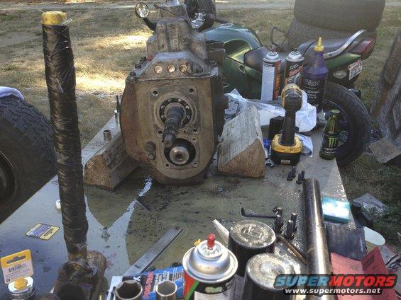 Transmission and driveshaft parts laid out on a table with a green motorcycle in the background
