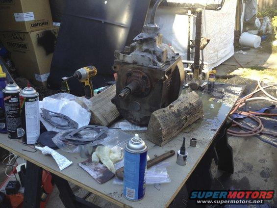 Transmission and parts laid out on workbench with tools and spray cans