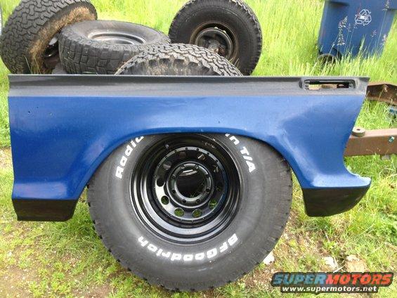 Blue truck bed panel with BFGoodrich Radial T/A tire and black rim. Other tires visible in background