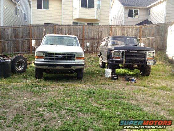 Black 1970s Ford Bronco with aftermarket bumper and white truck