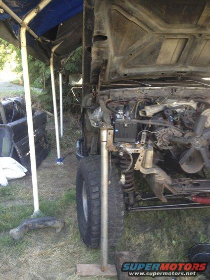 Engine bay with hood open, parts removed, under a canopy
