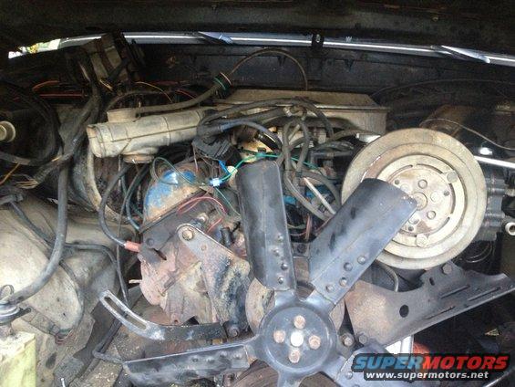Engine bay showing fan, AC compressor, and wiring. Some parts are rusted