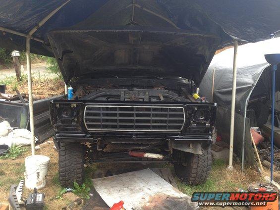 Front of a black 1979 Ford Bronco with hood open, parked under a tarp