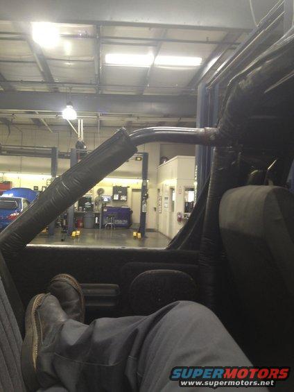 Interior view of a vehicle with padded roll bar and a person's legs and feet visible
