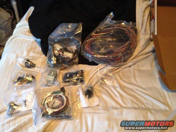 Several plastic bags containing vehicle wiring harnesses and electrical components laid out on a bed