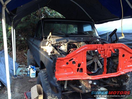 Front of a 1979 Ford Bronco with its hood and grille removed, parked under a blue tarp