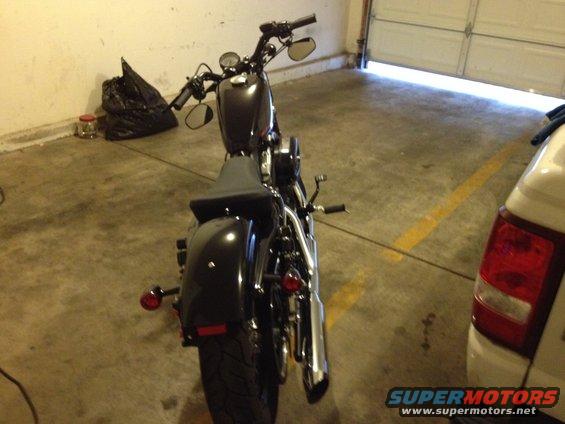 Black motorcycle parked in a garage, rear view. White vehicle to the right