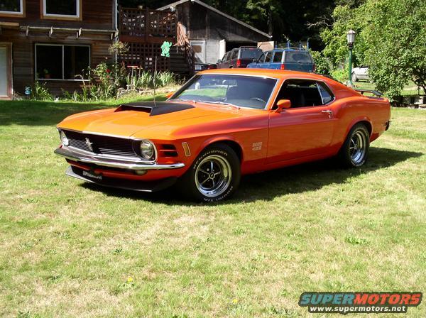 Orange 1970 Ford Mustang Boss 429 parked on grass in front of a wooden house