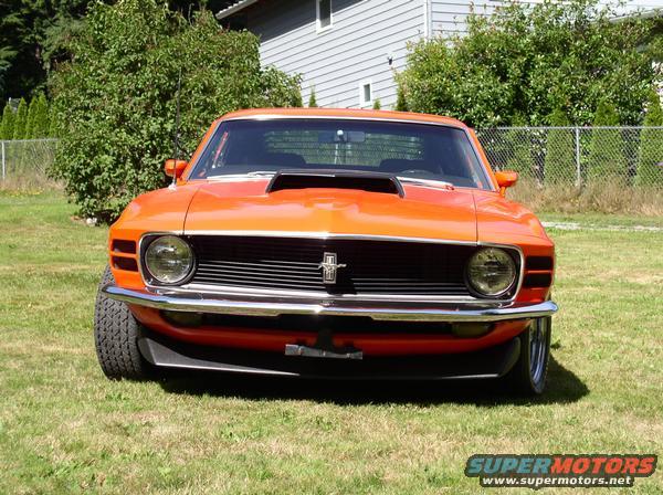 Orange Ford Mustang with hood scoop and chrome grille parked on grass