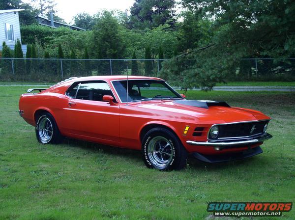Red 1970 Ford Mustang with a hood scoop parked on grass