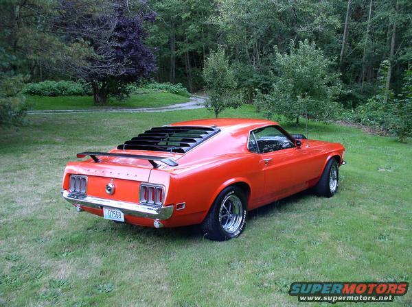 Orange 1970 Ford Mustang coupe with louvers and a spoiler, parked on grass
