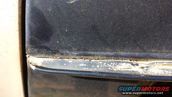 close-up of a dark blue vehicle's body panel seam with some rust and dirt