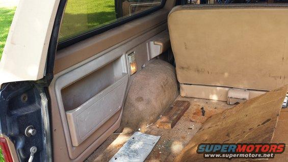 Tan interior of a 1980s SUV, showing a side door panel, rear seat, and cargo area with debris