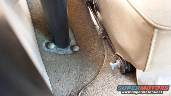 Close-up of vehicle interior showing carpet, seat base, and a metal support post bolted to the floor