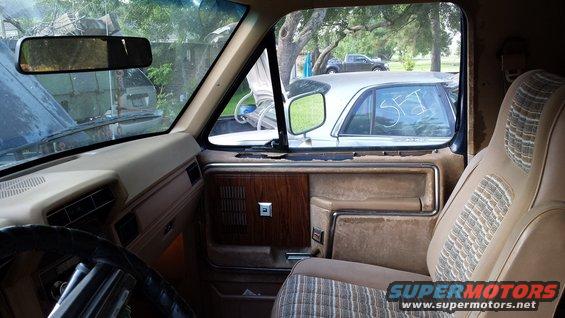 Interior of a tan truck with wood-grain door panel and patterned seat. A silver car is visible through the window