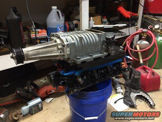 supercharger sitting on a blue bucket, with tools and gas cans nearby