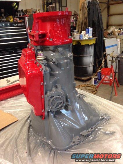 Gray and red painted transmission assembly on plastic sheeting in a workshop