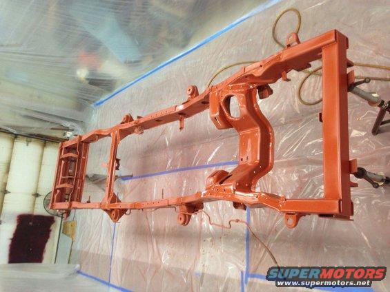 orange painted vehicle frame hanging in a spray booth