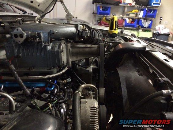 engine bay with supercharger, alternator, and fan shroud visible. Some hoses and wiring are present