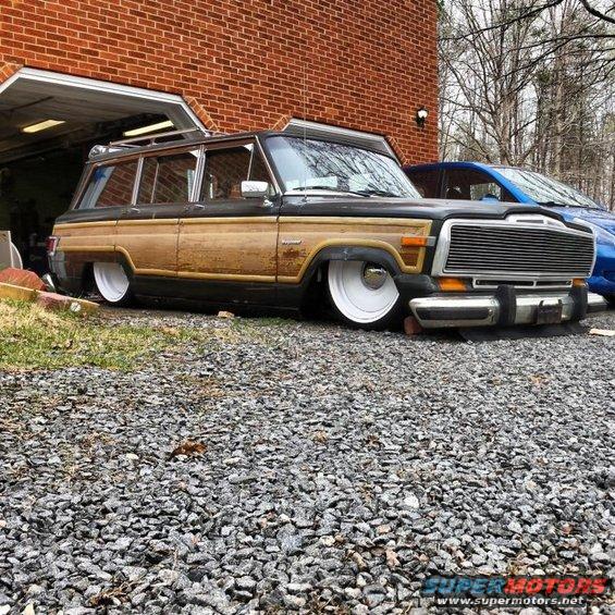 Wood-paneled station wagon, lowered, parked in front of a garage. Another car is visible behind it