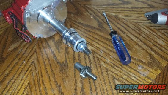 Red and silver distributor with a separate gear and a blue-handled screwdriver on a wooden surface