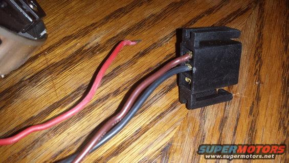 Black electrical connector with red, brown, and black wires attached, lying on a wooden surface