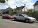 1999 Ford Fairlane - Two cars, a silver sedan and a red Ford Mustang, are parked on the side of a street in front of houses.