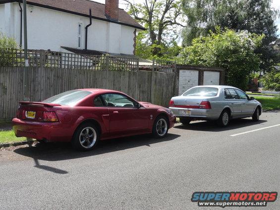 Red Ford Mustang coupe and silver sedan parked on a residential street