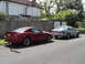 1999 Ford Fairlane - Two cars are parked on the side of a street in front of a house and garages.