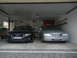 1999 Ford Fairlane - A silver sedan is parked in a garage next to a black Audi, with a map mural on the back wall.