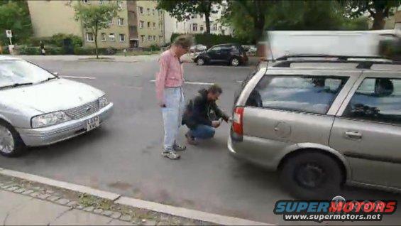 Two men near a silver station wagon and a silver sedan on a street