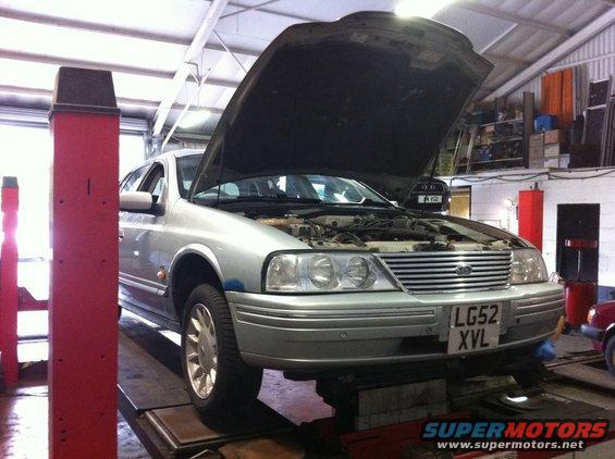 Silver sedan on lift, hood open, license plate LG52 XVL