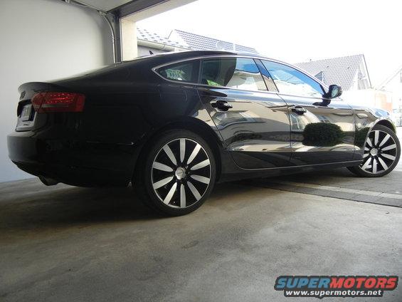 Black sedan, rear 3/4 view, custom wheels
