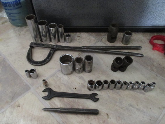 Assortment of sockets, wrenches, and a punch tool on a tiled floor