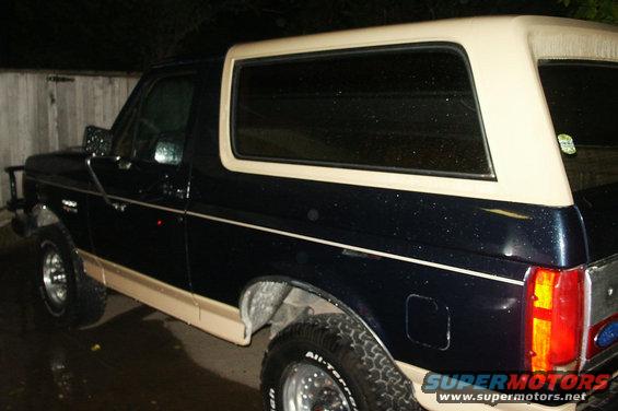 Dark blue Ford Bronco with tan trim and a tan removable top, seen from the side at a 3/4 front angle
