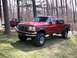 1996 Ford F-250 - A red 1996 Ford F-250 crew cab pickup truck with large tires is parked on a grassy area with trees in the background. Another red truck is…