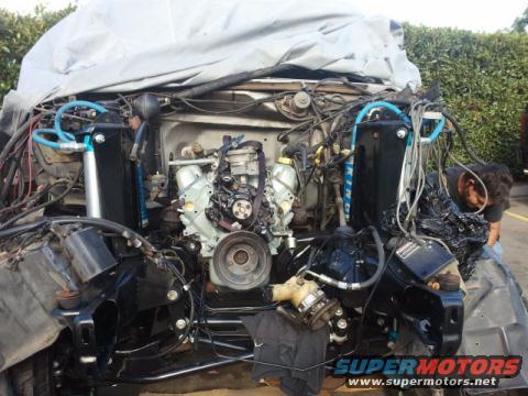 Vehicle engine bay with engine partially visible under a tarp, complex wiring and plumbing