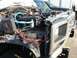 1986 Ford Bronco - The engine bay of a silver Ford Bronco shows exposed wiring and blue hoses, with another vehicle visible behind it.