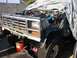 1986 Ford Bronco - A 1986 Ford Bronco is partially covered, revealing its front grille and exposed engine bay.