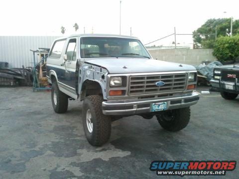 Silver and blue Ford Bronco with front fender removed, lifted suspension, and aftermarket wheels