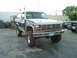 1986 Ford Bronco - A two-tone Ford Bronco sits in a lot with its front fender missing and a second vehicle visible in the background.