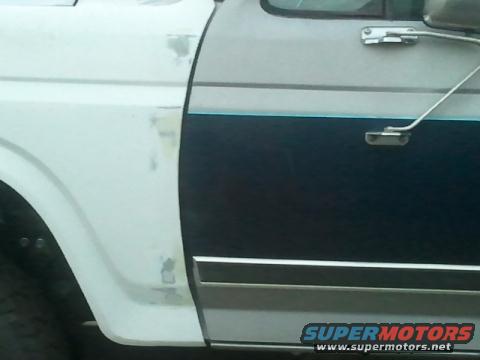Side view of a white fender and dark blue door with chrome trim on a Ford truck, showing bodywork