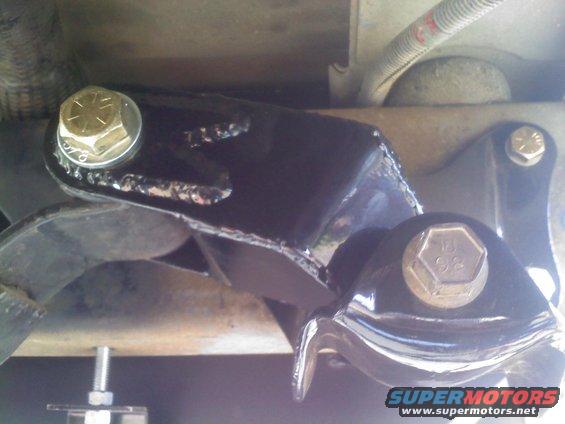 Black painted metal bracket with gold bolts, part of a vehicle's suspension system