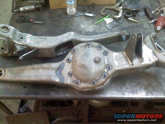 Two metal automotive rear axle assemblies sit on a workbench with tools scattered around