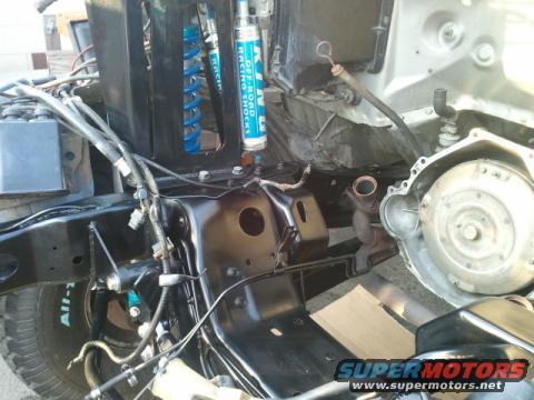 Vehicle chassis with engine components, blue racing shocks, and wiring. Tire with text visible
