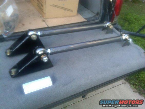 Two black metal suspension arms with silver ball joints rest in a vehicle bed